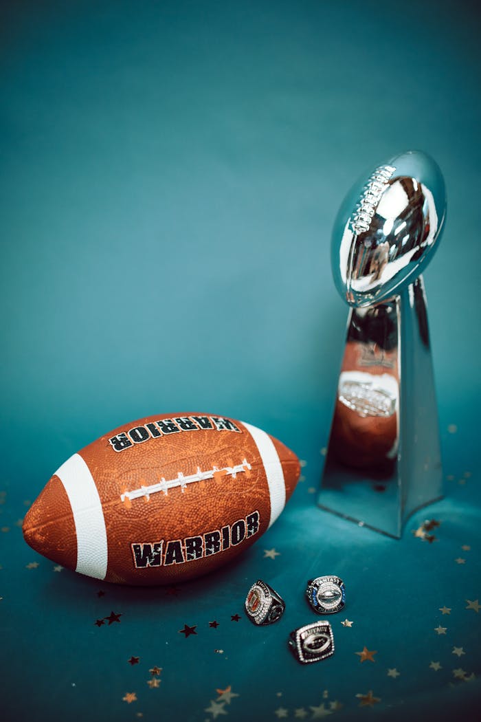 Football trophy and rings with a football on blue background, symbolizing victory and achievement.